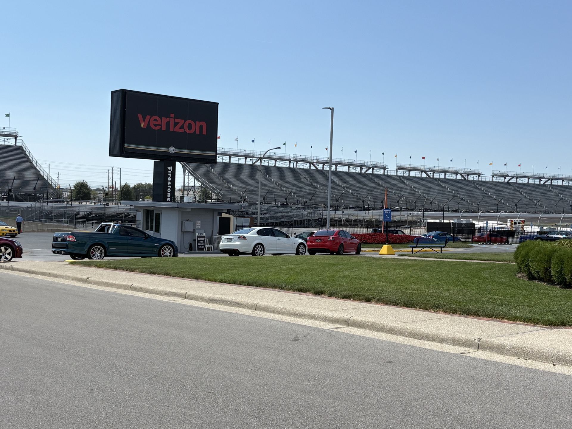 Verizon sign and grandstands at Indianapolis Motor Speedway with cars parked in the lot
